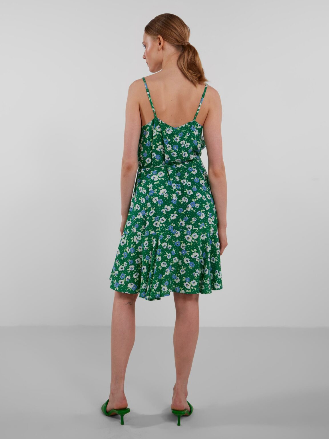 Modelo de espaldas con un vestido floral verde de tirantes.